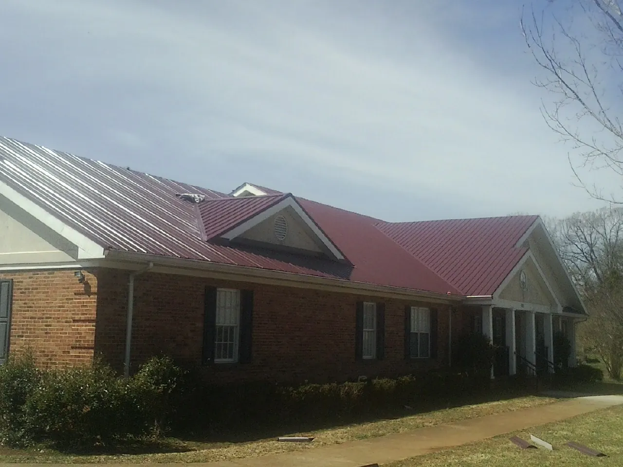 Red metal roof with gabled entries on a long brick building, from a Hail Damage Roof Repair job in Pine