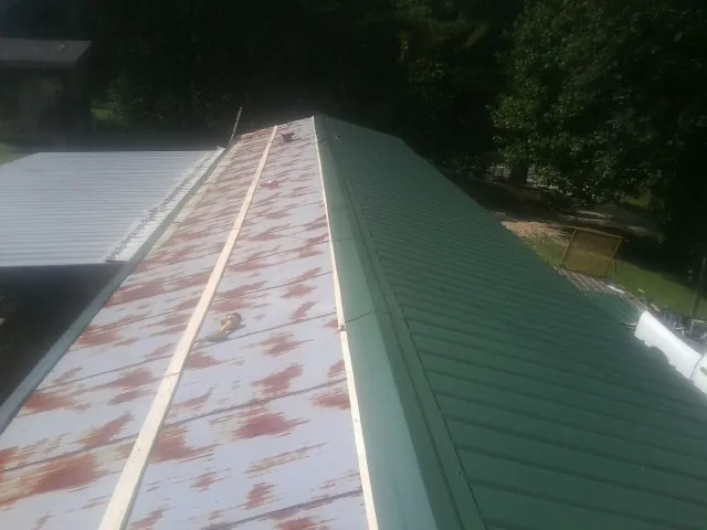 Old rusted panels beside newly installed green metal roofing — Wind Damage Roof Repair by Roofing Brothers in Pine
