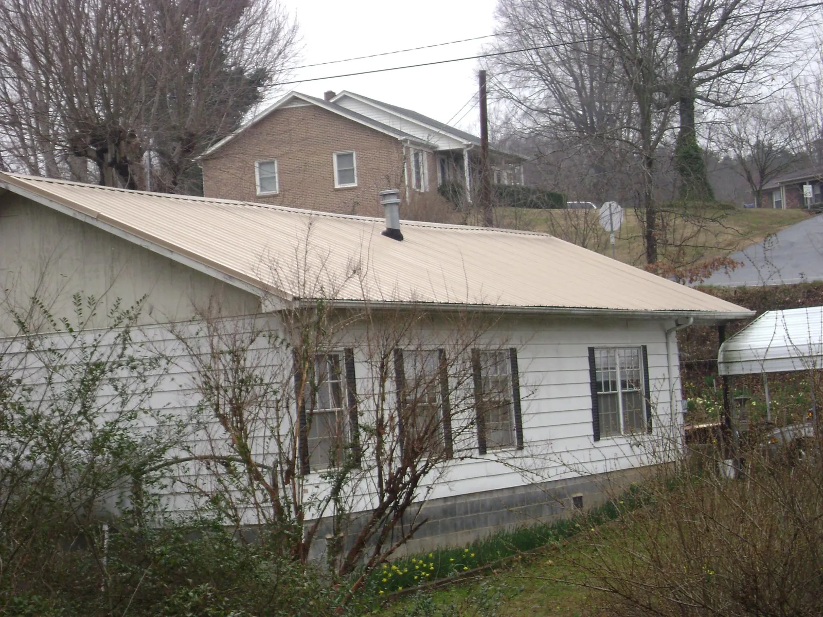 Tan metal roof on a white sided house set into a hillside — Commercial Roofing by Roofing Brothers in Pine